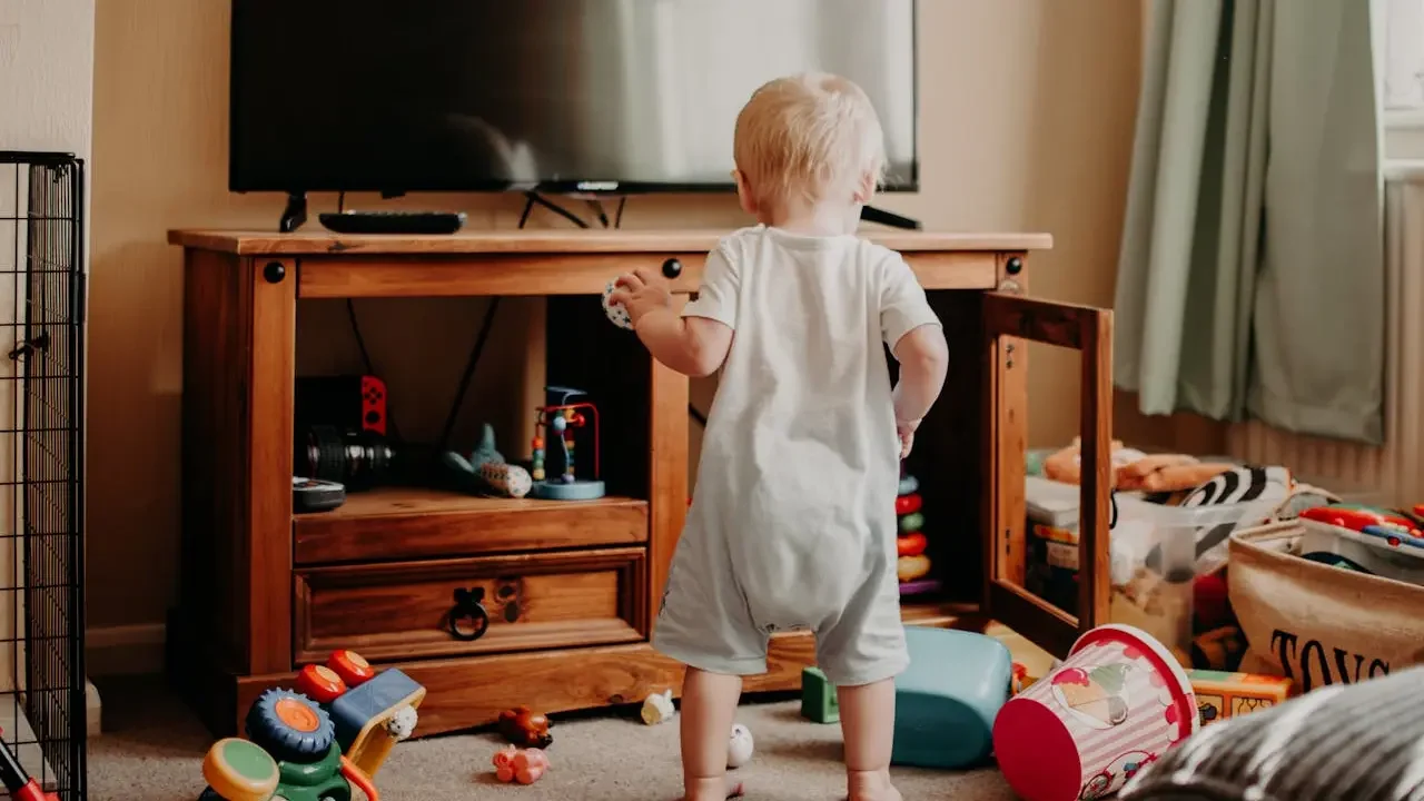 Bebê caminha pela sala com TV ao fundo