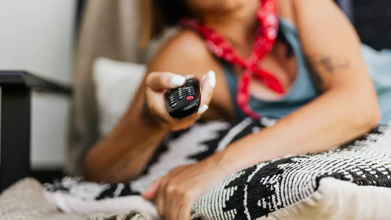 Detalhe mulher em primeiro plano com controle remoto